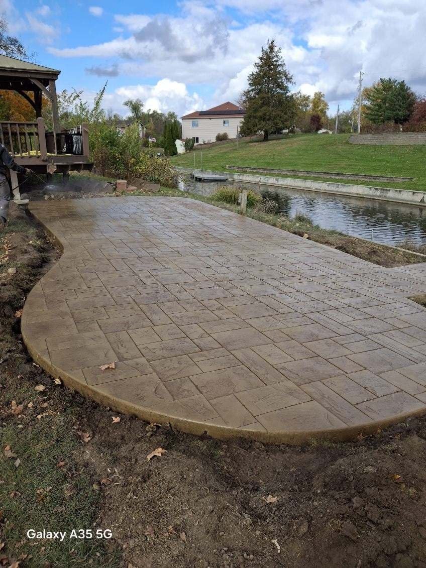 Newly installed brown stamped concrete patio with a curved edge next to a backyard canal.