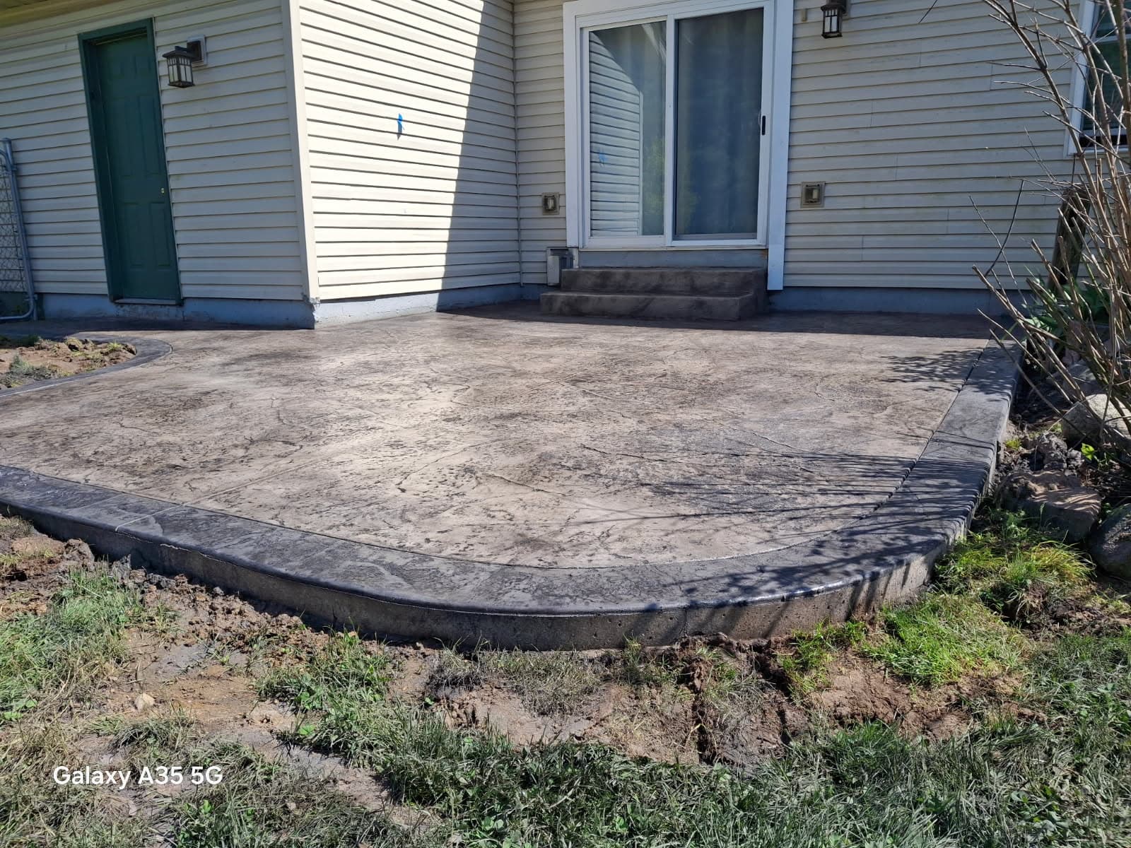 Textured stamped concrete patio with a dark gray border behind a light-colored residential house.