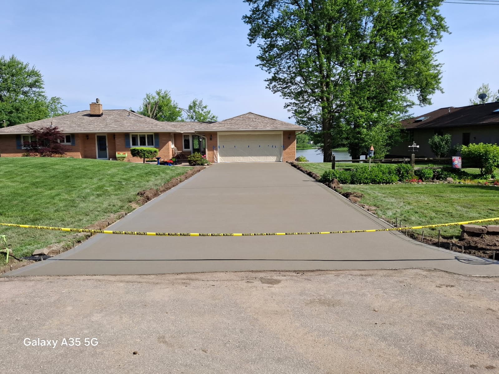 Freshly poured concrete driveway cordoned off with yellow caution tape before a brick home.